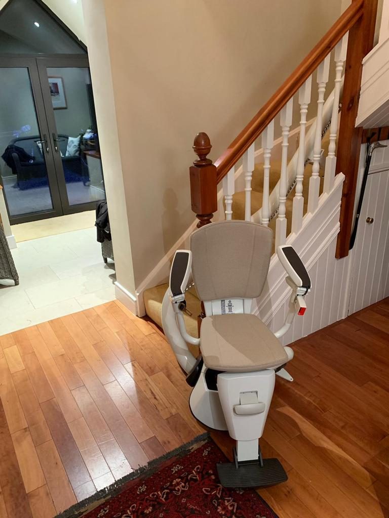 Stairlifts in Northern Ireland: Curved stairlift with a grey seat at the foot of a staircase in a family hallway