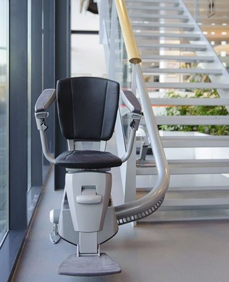 Maintenance Guides for Stairlift Supply: Curved stairlift with black upholstery at the foot of an open-tread staircase in a commercial building
