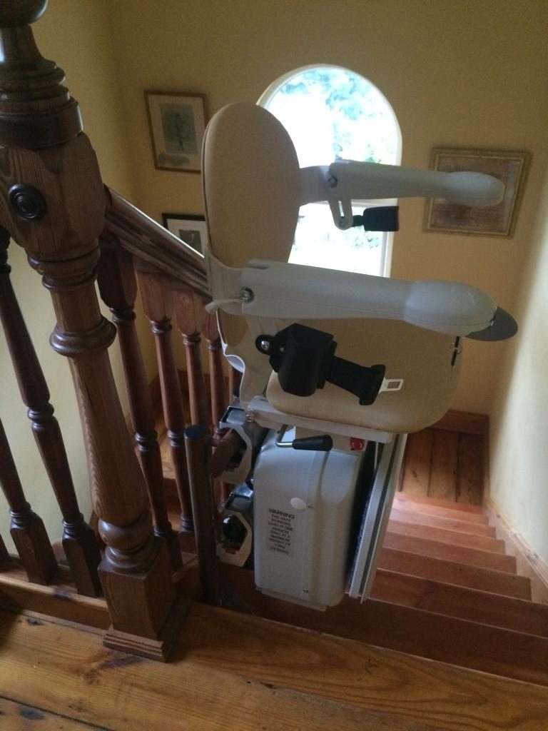 Stairlifts in Northern Ireland: Stairlift with its arms folded at the top of a wooden staircase beside a traditional newel post
